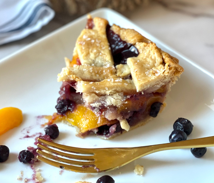 https://mirjamskitchenyodel.com bite taken from a slice of blueberry peach pie