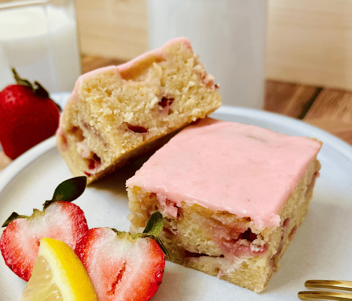 https://mirjamskitchenyodel.com/strawberry blondies/ on a plate with decorative strawberries and lemon